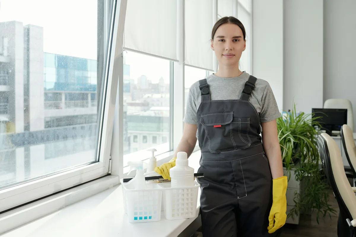 Person holding a basket of cleaning products beside an office window