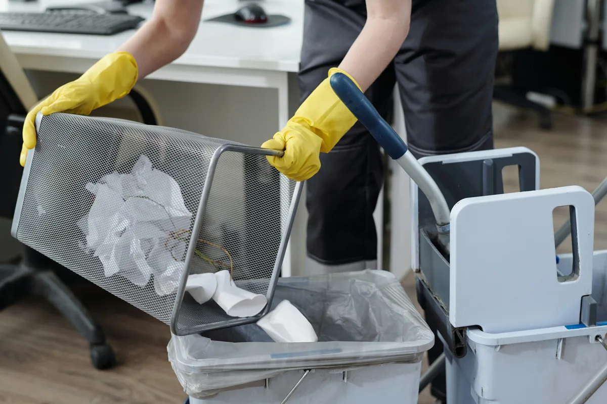 Gloved hands organizing cleaning equipment and supplies on a cart