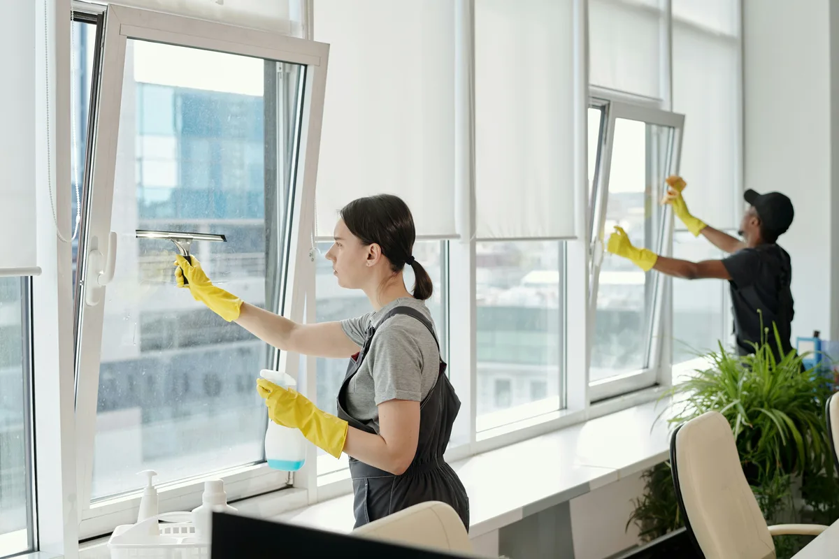 Gloved hands wiping an interior office window with a cloth