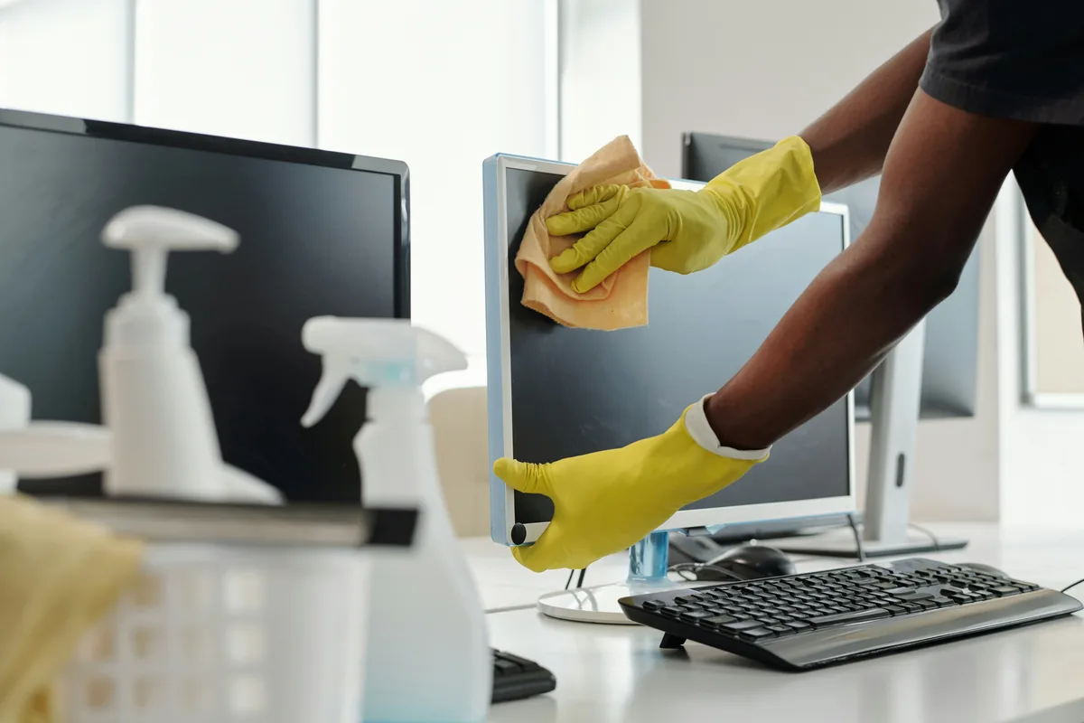 Gloved hands wiping an office monitor beside a keyboard