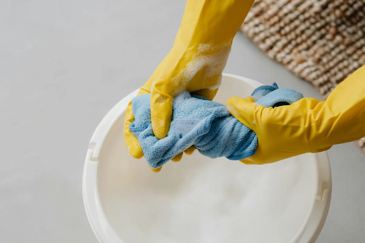 Protective gloves holding cleaning cloths over a bucket