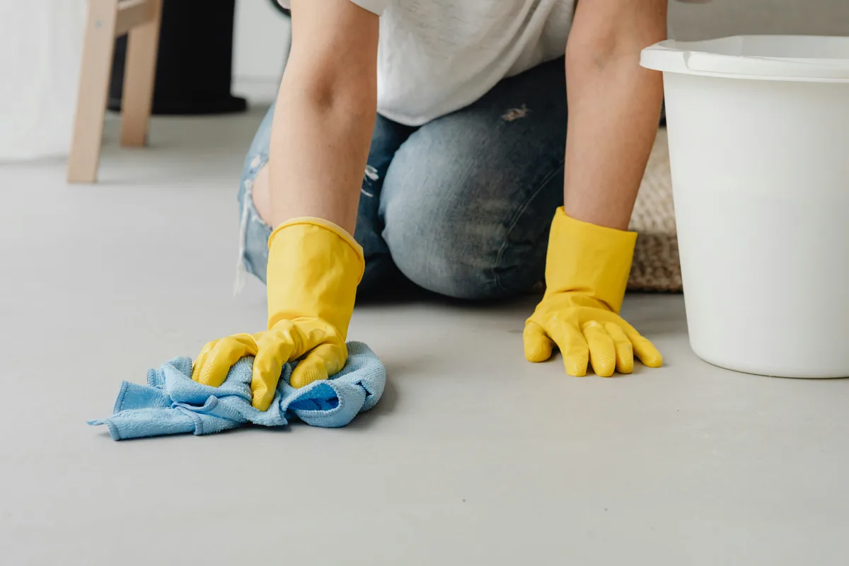Person kneeling to wipe a floor with a cleaning cloth