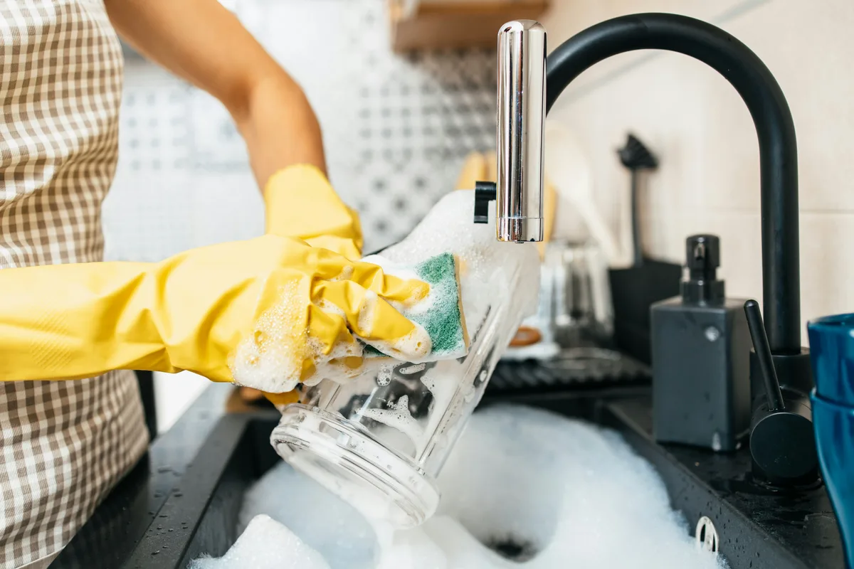 Person rinsing a glass at a kitchen sink