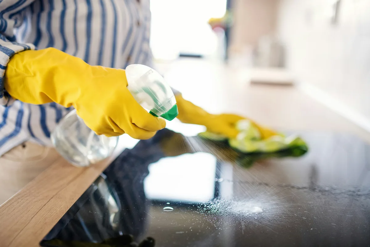 Gloved hands spraying and wiping a kitchen cooktop