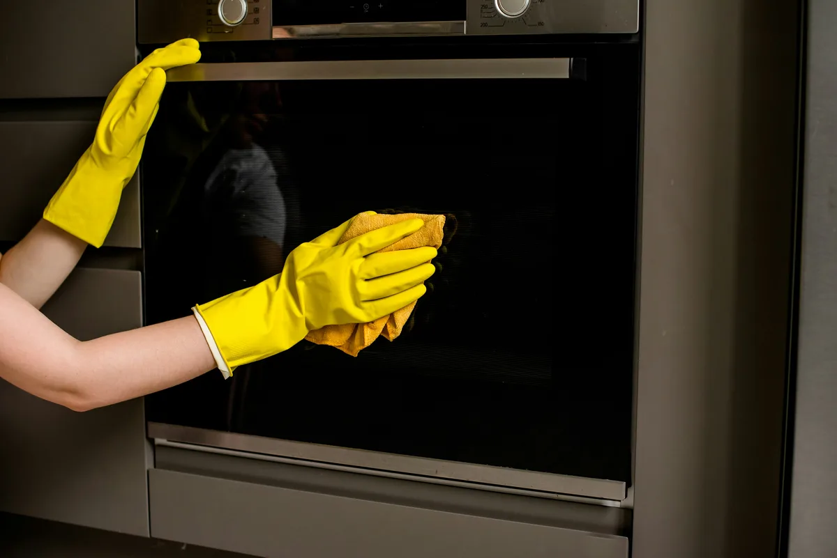 Person wiping the inside of an oven with protective gloves