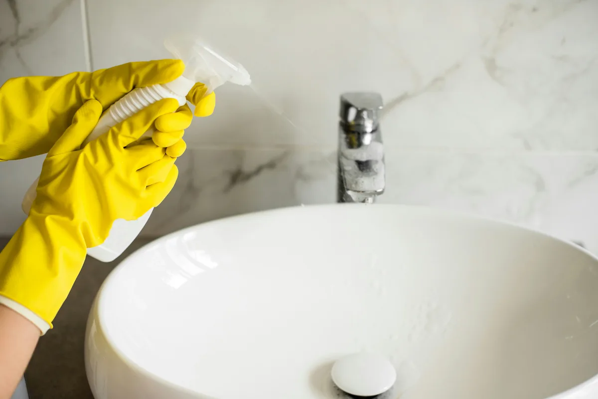 Gloved hand polishing a bathroom faucet above a basin