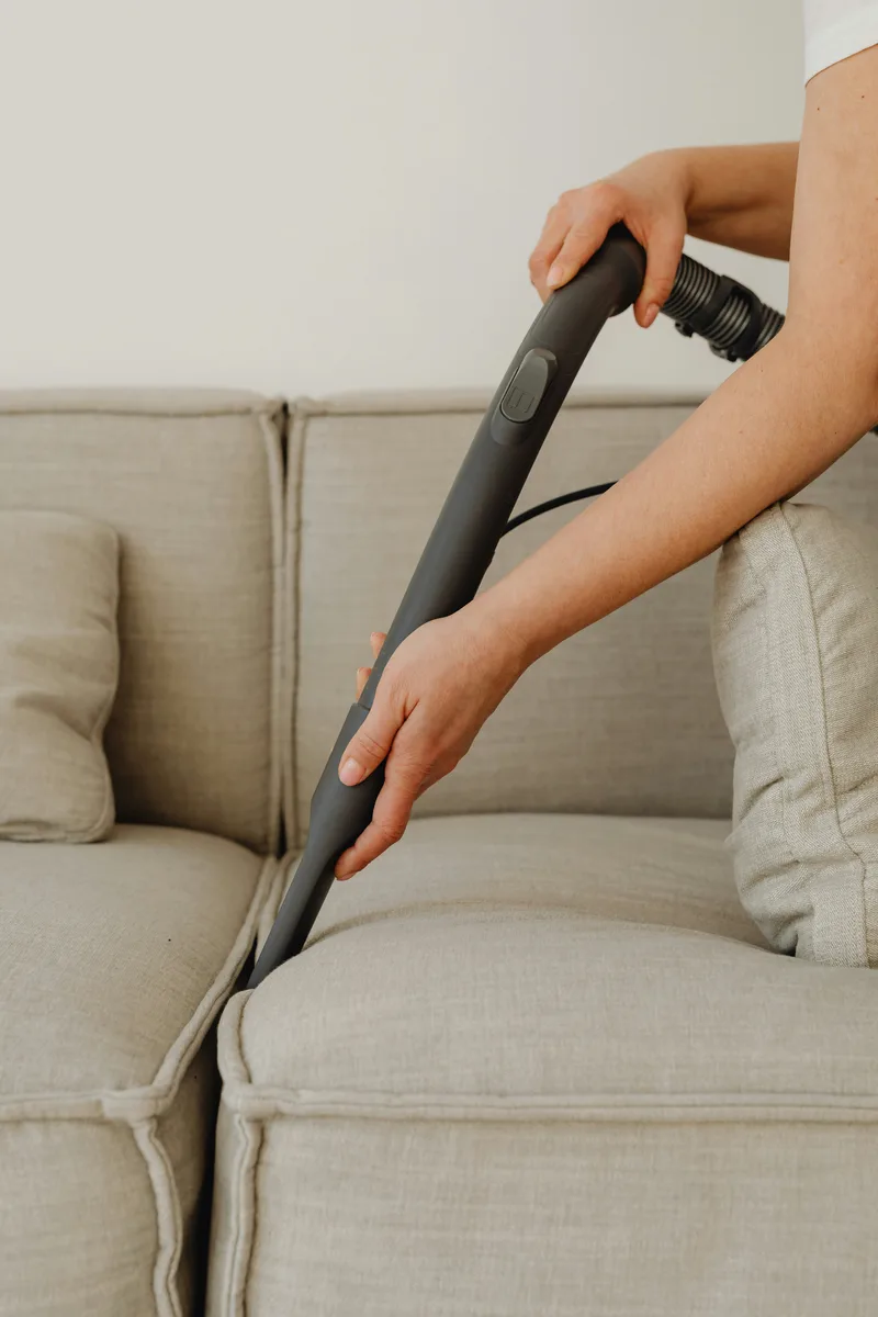 Person vacuuming sofa cushions as part of a regular cleaning